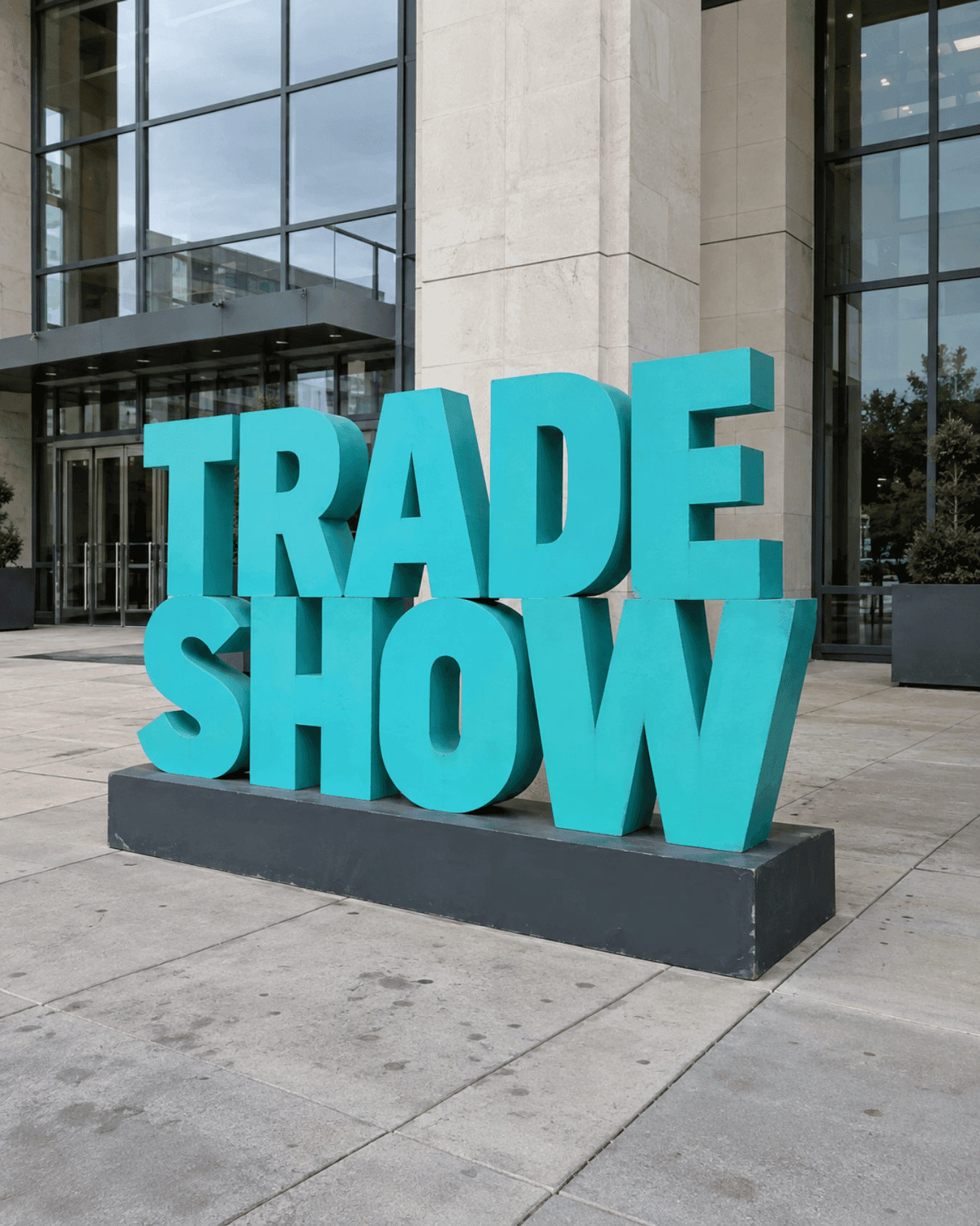 Stacked teal TRADE SHOW letters on a gray display base