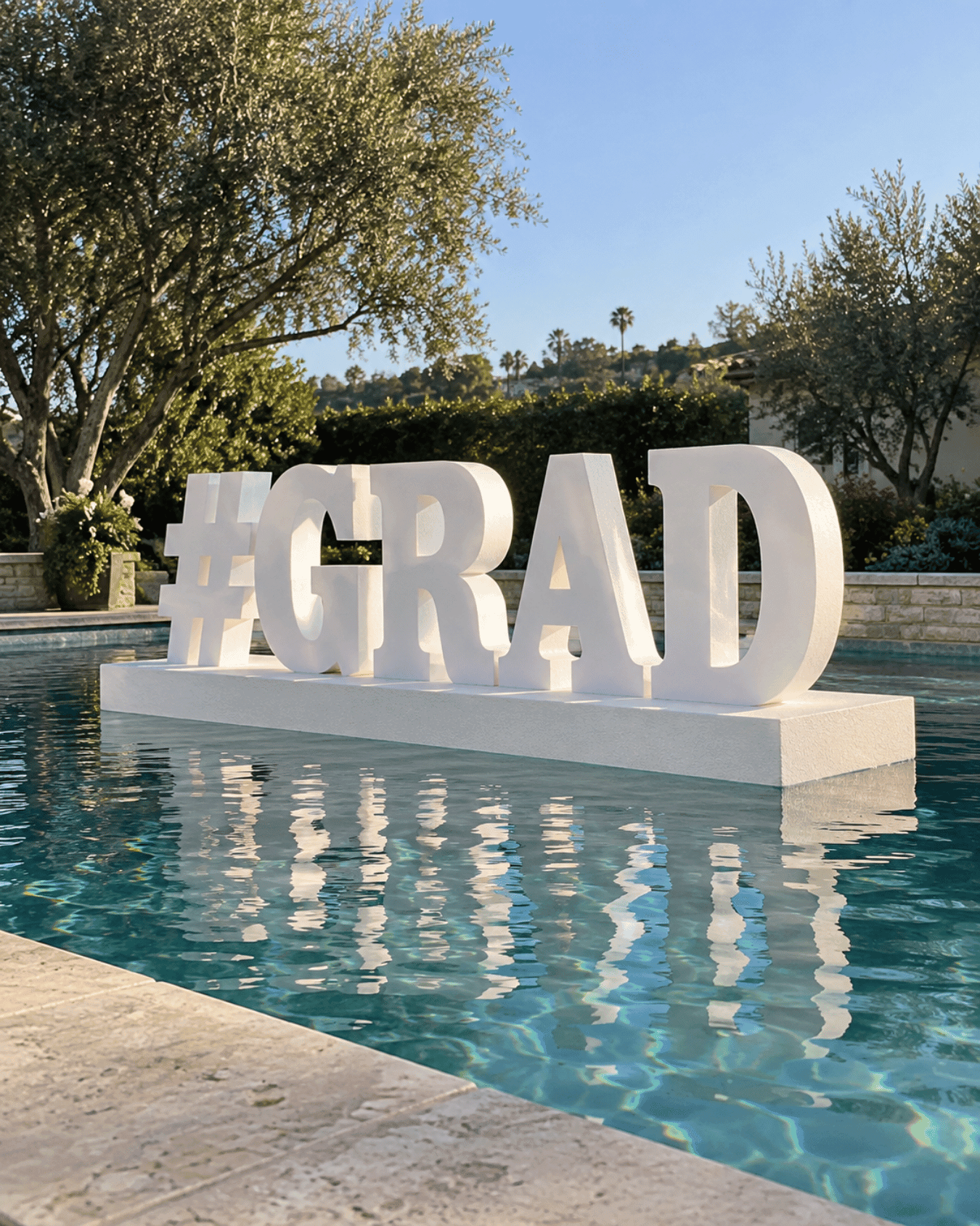 White GRAD letters on a display base beside a swimming pool