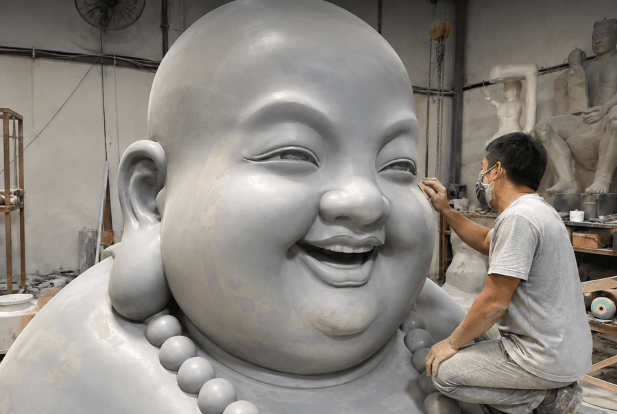 Craftsperson beside a large silver laughing Buddha sculpture in the workshop