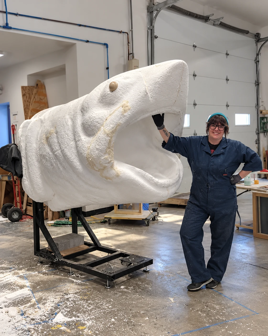 Person standing beside an oversized white foam shark head sculpture in a workshop, showing its scale